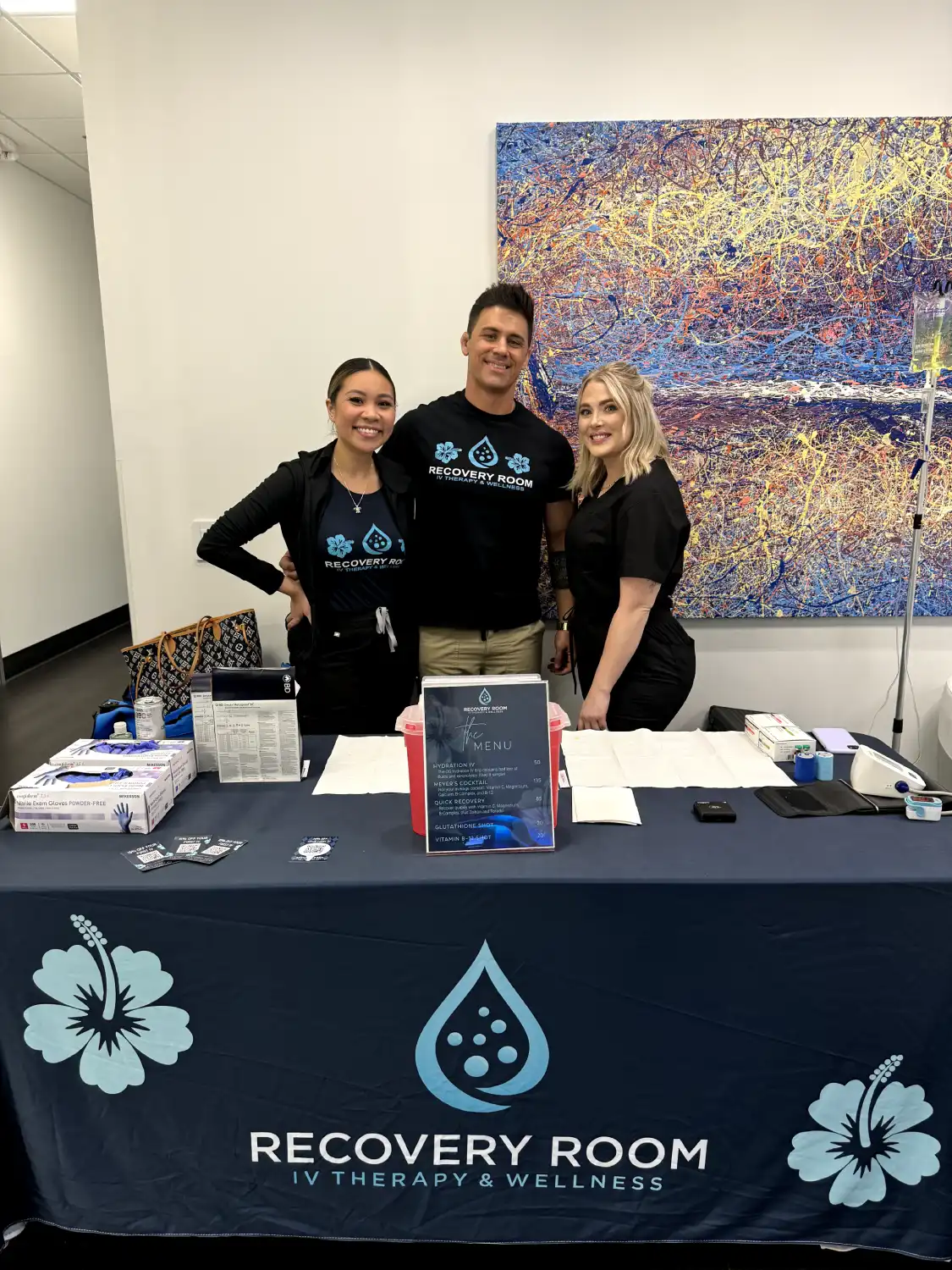 The Recovery Room AZ team at their branded treatment table with the IV therapy menu