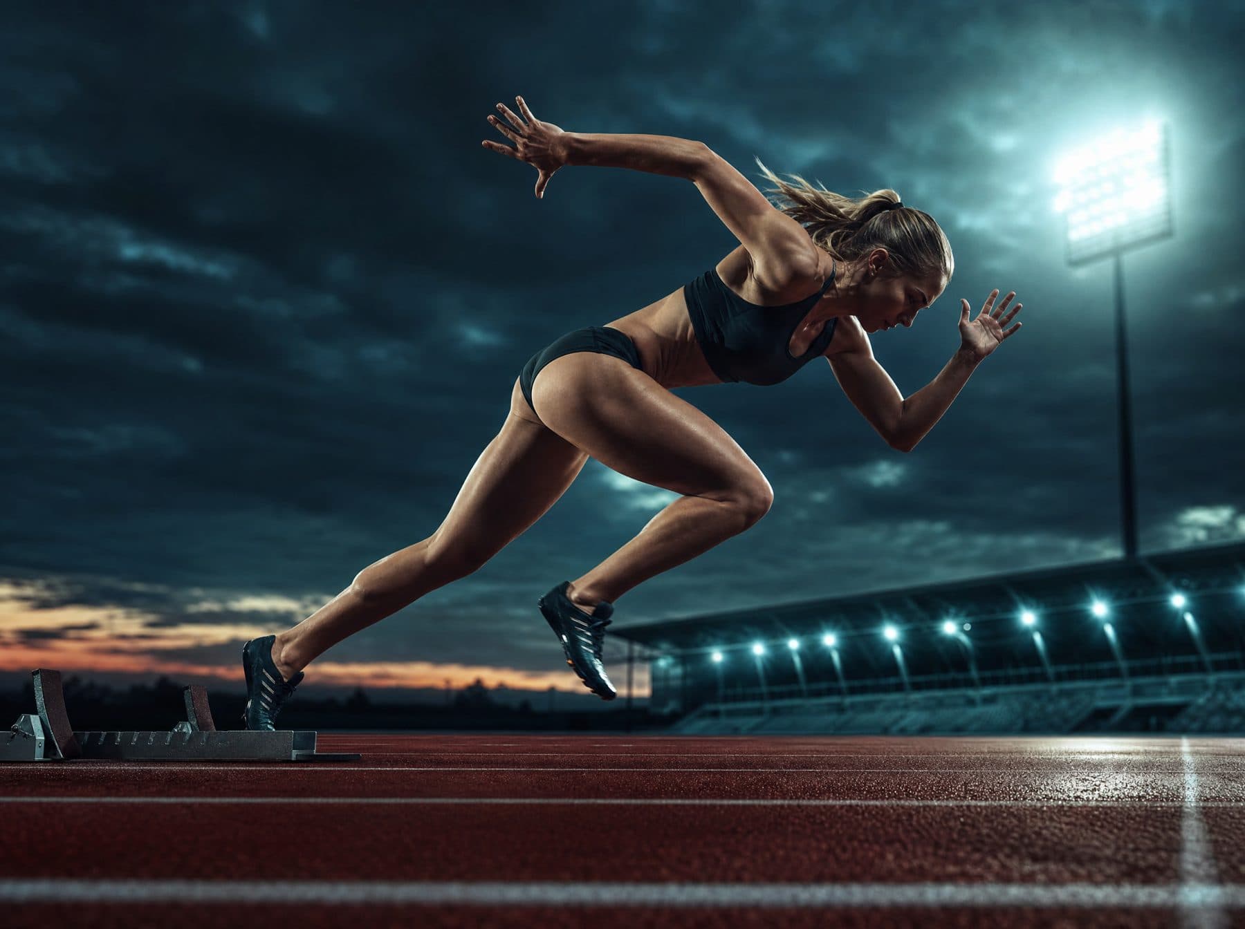 Sprinter driving off the starting blocks under dusk stadium lights