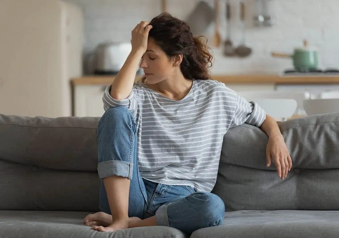 Woman on a couch holding her head while feeling unwell